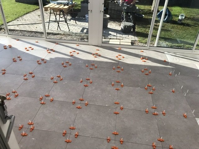 Installation av kakelgolv med orange distanser i ett uterum med stora glaspartier och utsikt över trädgården.