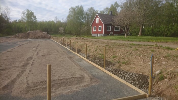 En nyförberedd paddock med nyligen uppsatta stolpar och sand, med ett rött hus i bakgrunden.