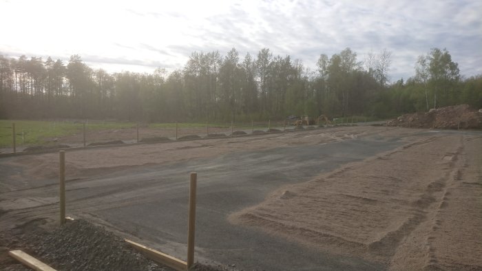 Byggarbetsplats för en paddock med uppryckta stolpar, utlagd sand, grus och en grävmaskin i bakgrunden.