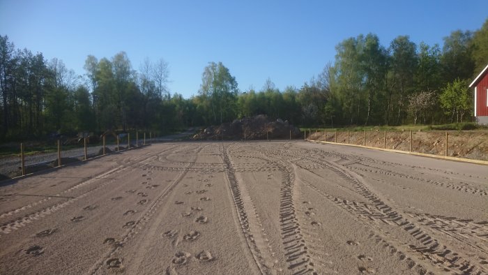 Nyplanerad paddock med uppryckta stolpar och en hög jord i bakgrunden, spår av entreprenadmaskiner.