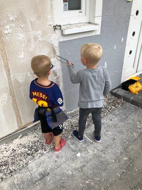 Två barn står framför en putsad husvägg och en av dem håller i en spackelspade.