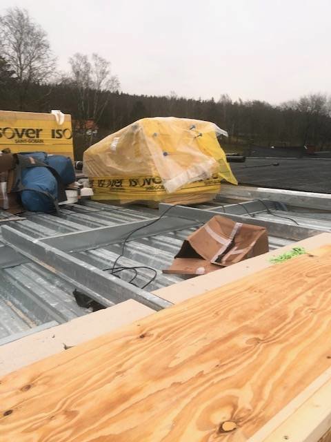 Obyggd husgrund med temporär plywood och isoleringsmaterial, omgiven av byggmaterial under bar himmel.