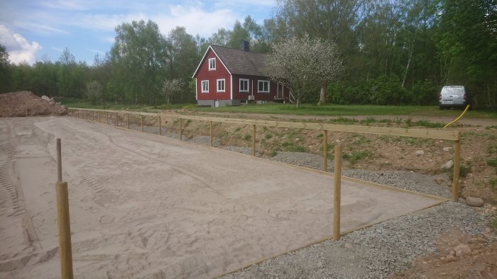 Stomme till paddock med stolpar och makadam underlag framför ett rött hus med vitmålade knutar och blommande äppelträd.