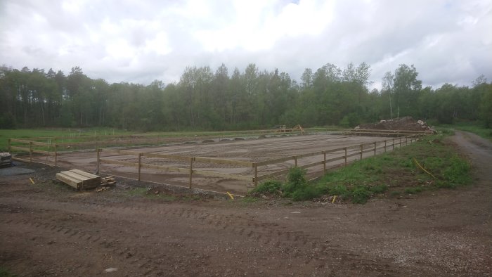 Byggarbetsplats för en paddock med halvfärdigt stängsel och grovplanerad mark under molnig himmel. Traktor i bakgrunden.