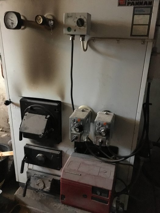 Begagnad pelletsbrännare med reglage och manometer, i ett mörkt rum, diskussion om lämpligt märke och typ.