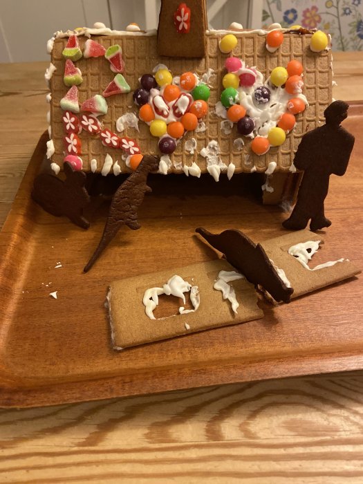 Pepparkakshus med skadat väggparti och figuriner av dinosaurier och människor.