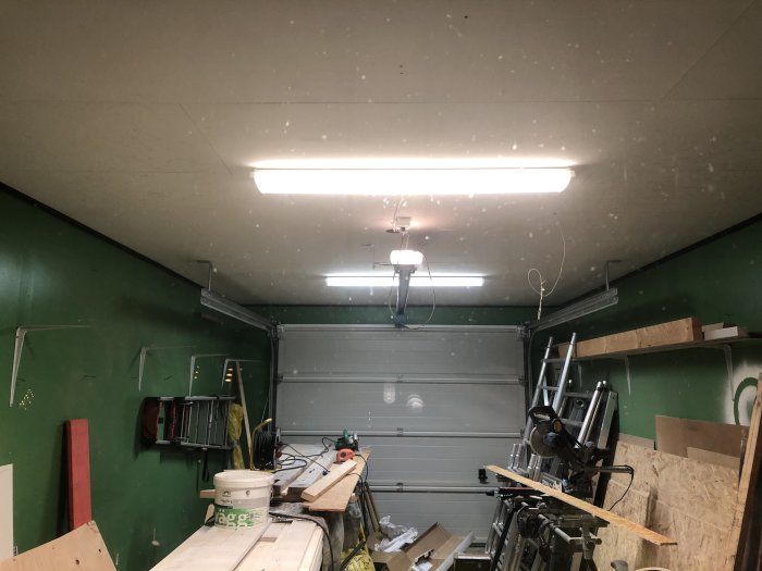 Garage med nyinstallerade lysrör i taket med olika färgtemperaturer, arbetsbänk och verktyg.