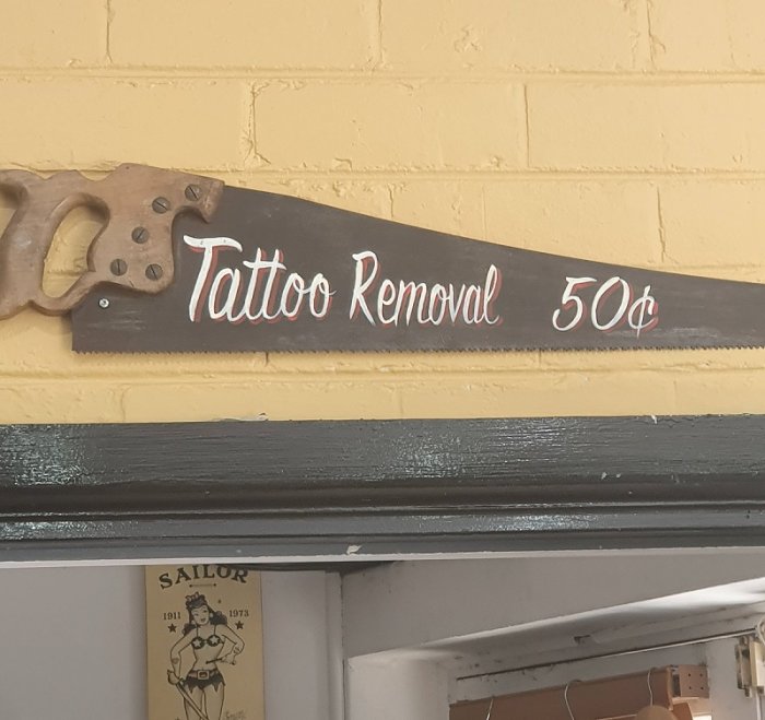 Handsåg omgjord till skylt med texten "Tattoo Removal 50¢" på en gul vägg.