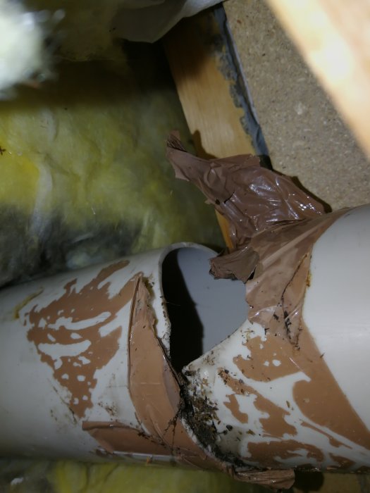 Söndrigt avluftningsrör lappat med packtejp och omgiven av isoleringsmaterial.