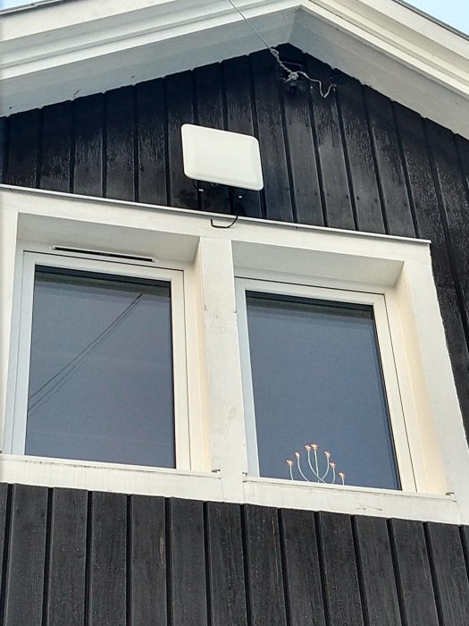 Nyinstallerad radiofiberantenn ovanför ett fönster på en mörkfärgad trävägg.