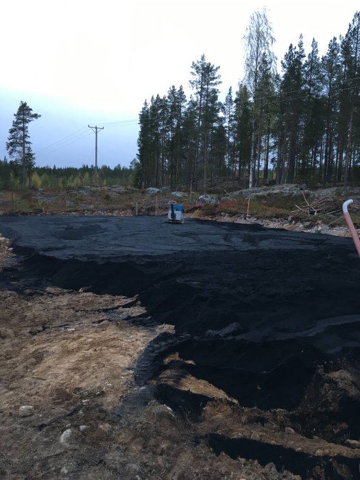 Markarbeten med geotextil på skogsmark inför byggprojekt, grävmaskin i bakgrunden.