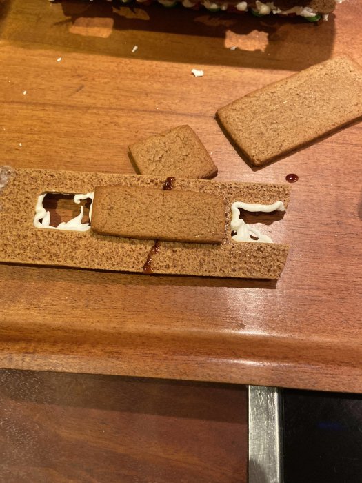 Pepparkaksbitar med kristyr, simulerar byggprojekt med balk och skorsten på ett bord.