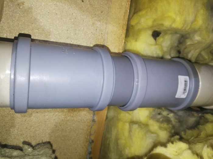 Ett PVC-rör med två skjutmuffar installerat bland isoleringsmaterial, visar en avslutad rörinstallation.