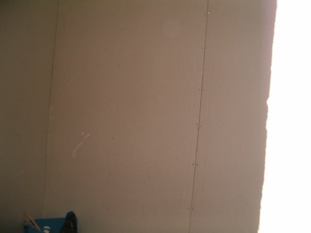 Vägg under renovering med ommålad gipsskiva och synliga skruvar.