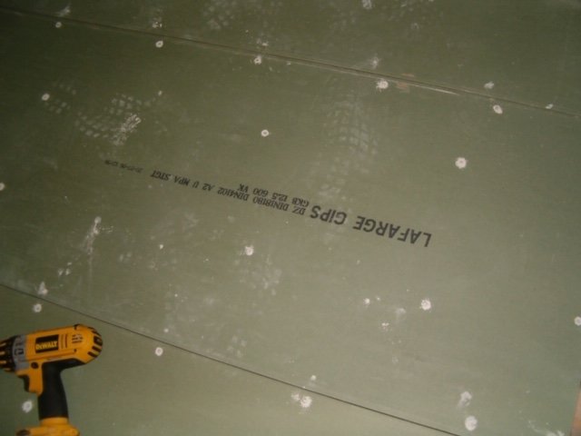 Gipsvägg med spackel och gipsband vid skarvar, samt en gul och svart skruvdragare i förgrunden.