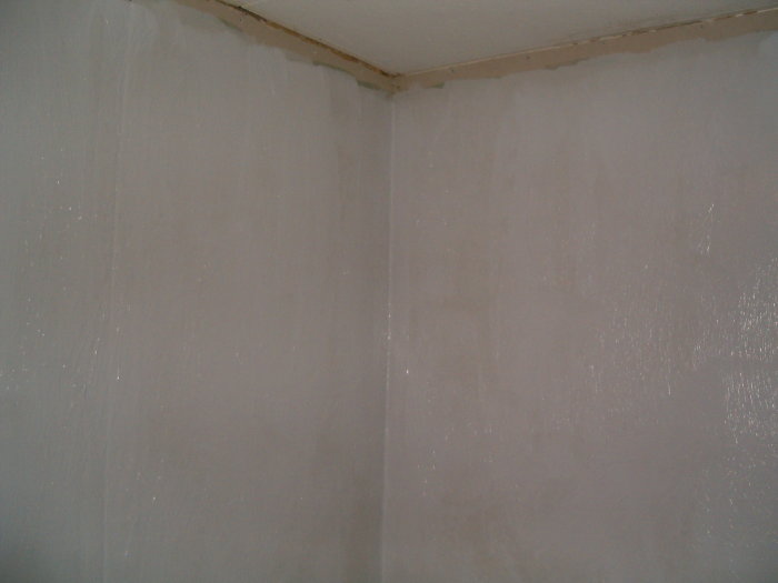Inre hörn av ett rum under renovering med nyligen spacklade och slipade väggar före målning.