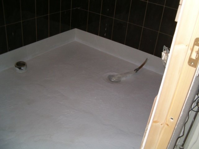 Nyinstallerad duschgolv med vattentätning och kaklade väggar i pågående badrumsrenovering.