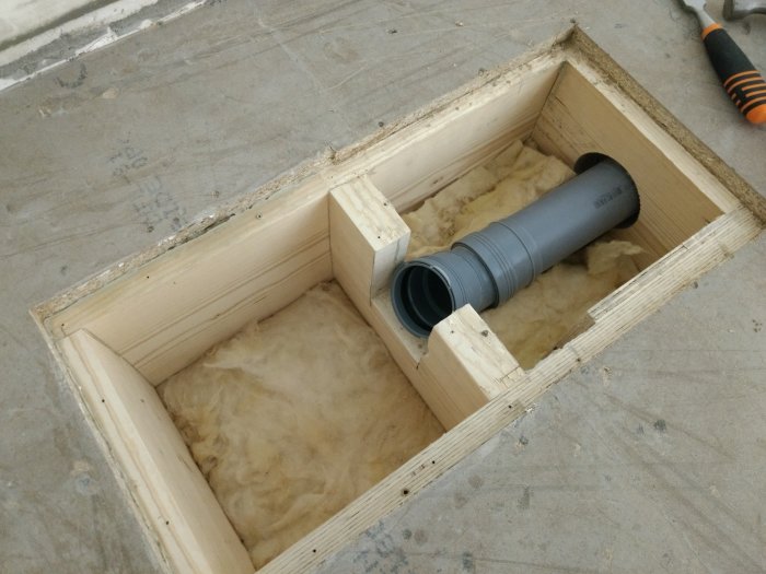 Öppet golv av betong med en kasserad öppning exponerande ett avloppsrör med böjar och en demonterad golvbrunn.