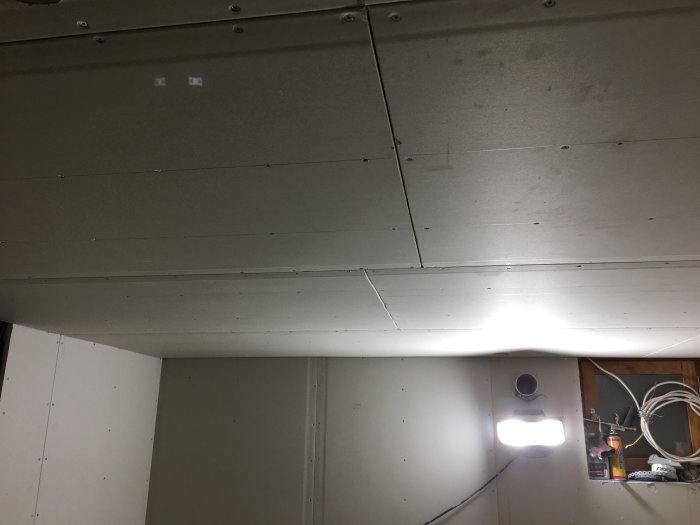 Nyinstallerade gipsskivor på tak med synliga skruvar och elkabel för spotlights.