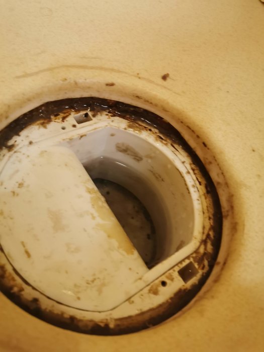 Bild på en skadad duschbrunn med lös ring och tecken på vattenläckage under golvbeläggningen.