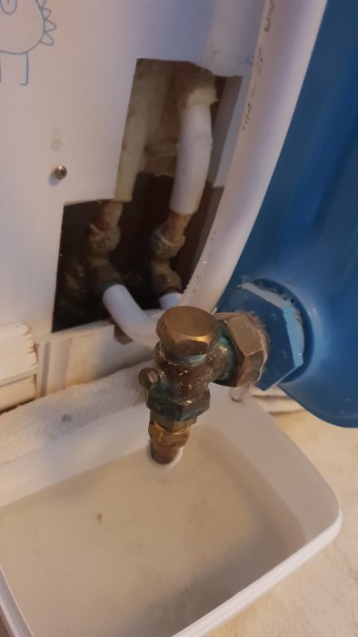 Element med avtaget lock och synlig justerskruv, med vatten som samlas i en behållare nedanför.