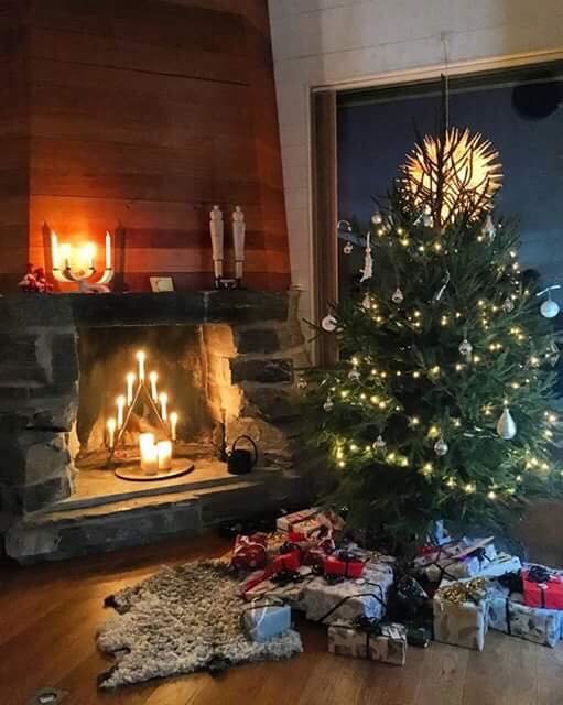 Öppen spis med skifferstenar och eld, julgran med ljusslinga och julklappar framför, byggd i Åre.