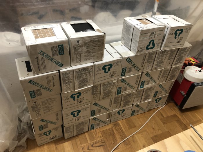 Staplar av vita och svarta kakelplattor i kartonger på ett trägolv med matt yta, redo för försäljning.