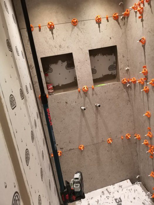 Badrum under renovering med korslaser som projicerar linjer på kaklade väggar och avståndskilar.
