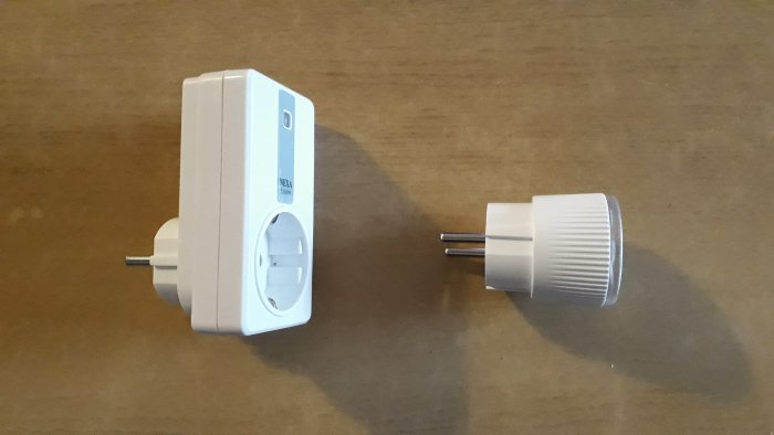 Ny smart plug jämfört med gammal Nexa plug, båda oanslutna på ett brunt bord.