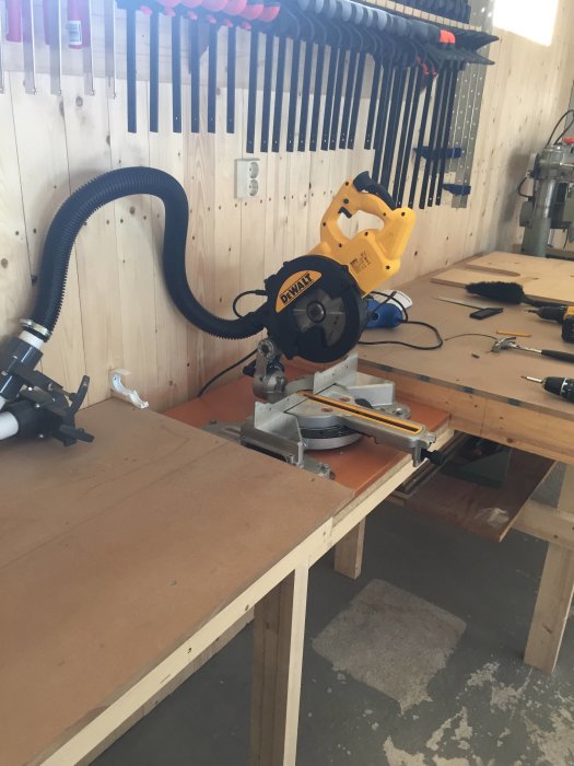Arbetsbänk med en kap- och gersåg, samt tvingar upphängda på en french cleat väggmontering i ett verkstadsutrymme.