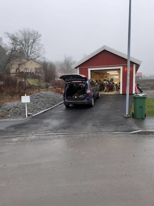 Nybelagd uppfart med bil framför öppet garage och grå himmel.