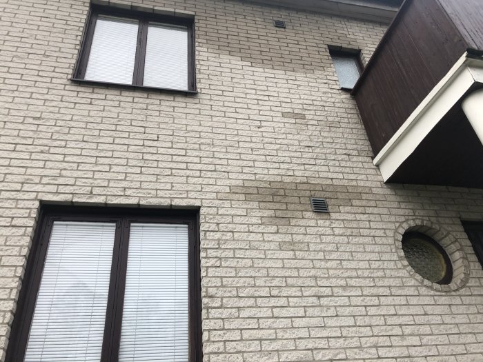 Ljus tegelfasad på en byggnad med vattenfläckar runt ett fönster och under en ventilationsöppning.