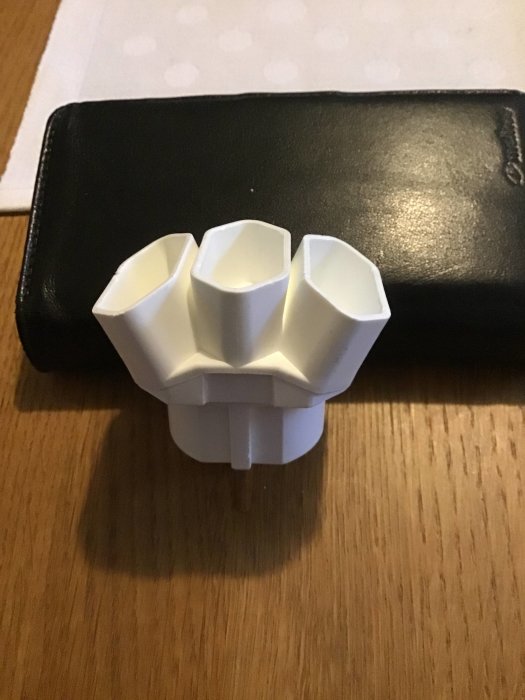 Vit grenkontakt med tre vinklade EU-uttag på ett bord med plånbok i bakgrunden.
