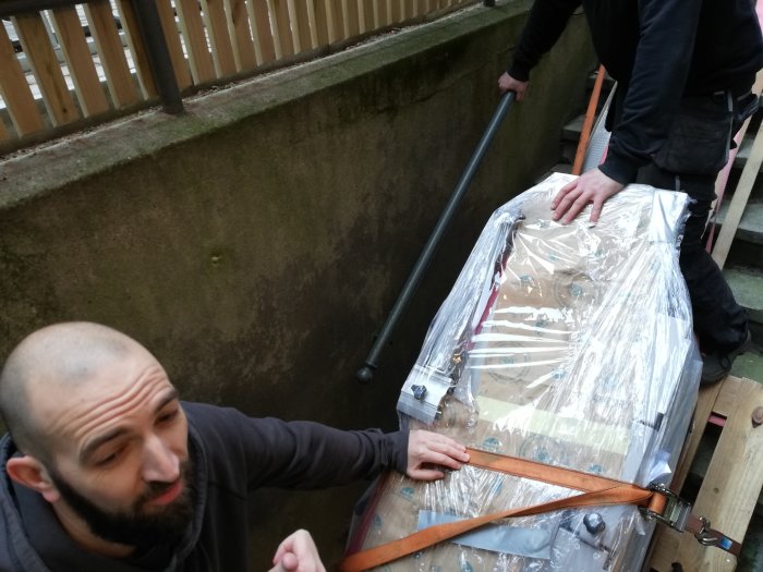 Personer som förbereder en maskin insvept i plast med spännband, en med fokus på uppgiften.