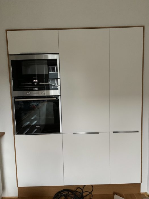 Vit köksinredning med flagnande färg på en kökslucka ovanför inbyggda ugnar.