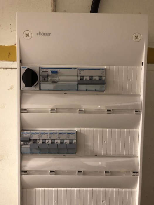 En nyinstallerad elcentral av märket Hager med kopplade säkringar och ledningar i ett garage.