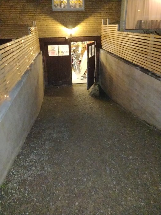 Vy genom en öppen garageport på natten, upplyst inuti, visar en trång infart och cyklar inuti garaget.