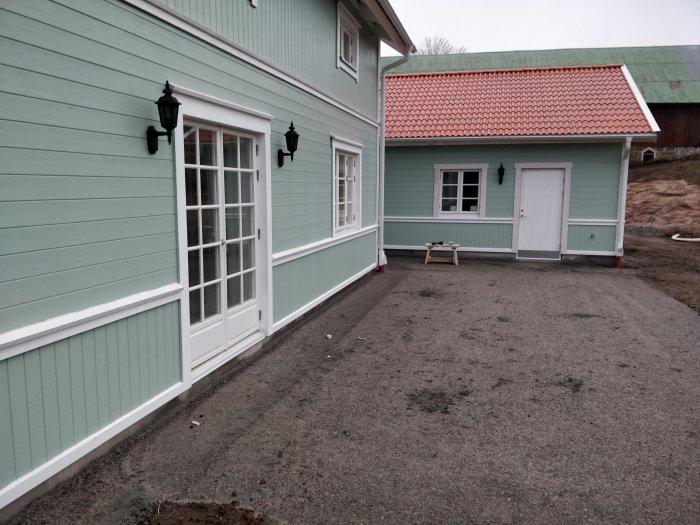 Nyinstallerade svarta utomhuslampor på en ljusgrön trävägg vid ett hus, grusgång framför.