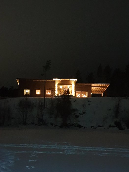 Ett nyligen färdigställt hus med tända fönster om natten, omgivet av snö och med outvecklad mark.