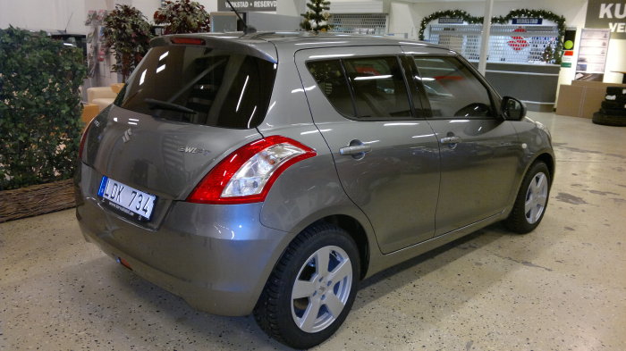 Grå Suzuki Swift, kallad ”Snyften”, i ett showroom, bakifrån höger perspektiv, utan synliga skador.