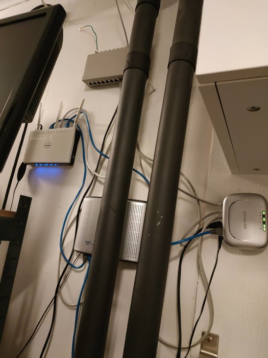 Trång nätverksinstallation med fiberoptik, switchar och rör mellan fönster och vägg.