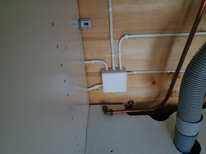 Lossnat varmvattenrör till vänster med synliga vattenledningar och träklädsel, tecken på vattenskada nära golvet.