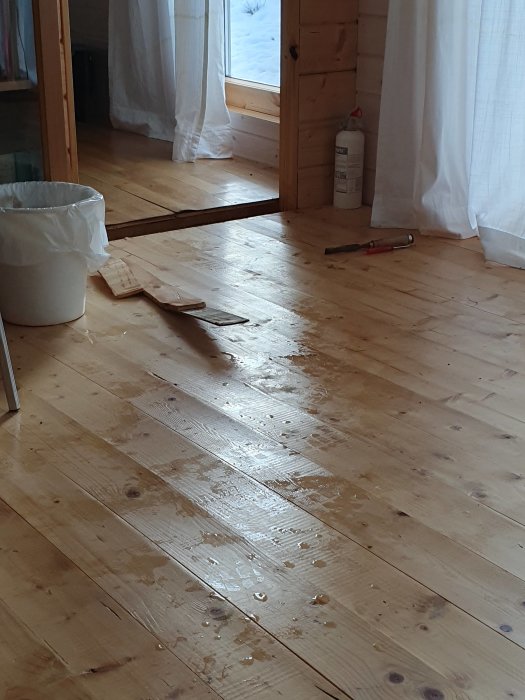 Våtrum med upplyft brädgolv och synlig vattenskada samt några verktyg på golvet.