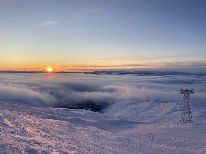 Soluppgång över ett dimtäckt Åresjön med skidliftar och snötäckta backar i förgrunden.