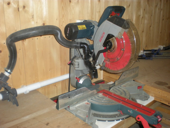 Bosch geringssåg installerad i verkstad kopplad till otillräckligt dammutsug med böjda slangar.