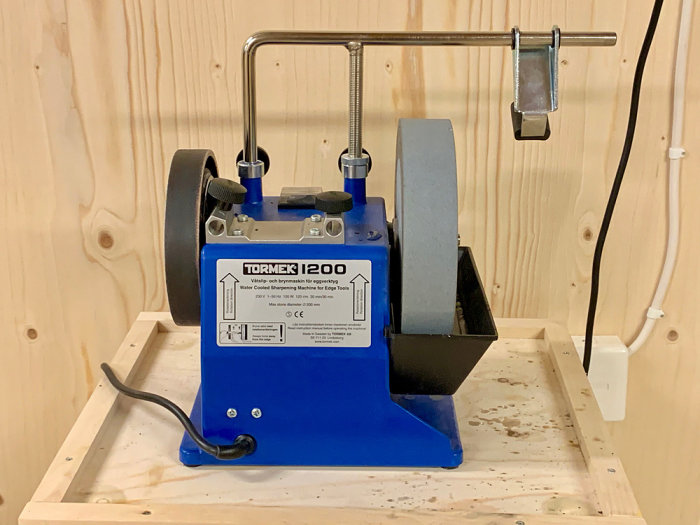 Oanvänd Tormek 1200 slipmaskin för verktyg, monterad på träbänk i ett förråd.
