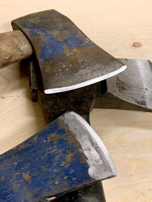 Slipade yxor med vassa eggar och slitage på skaften placerade på ett arbetsbord.