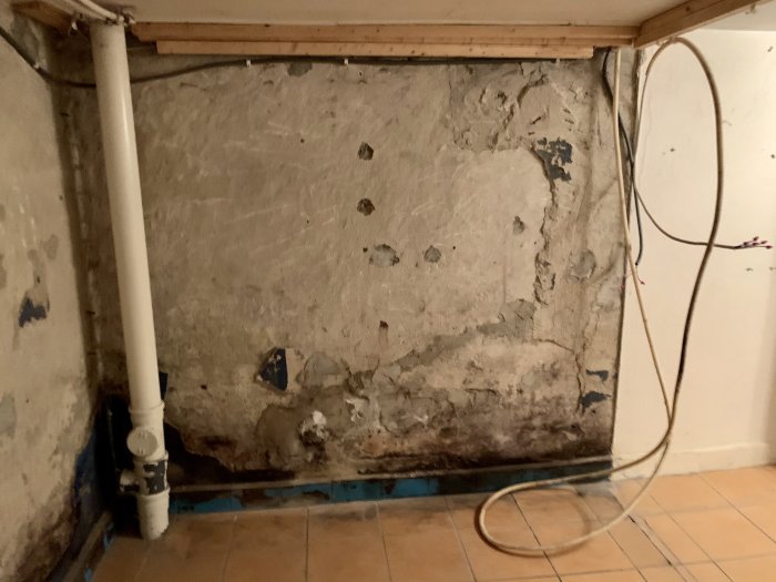 Gamla skadade väggar i källartvättstuga med behov av renovering och putsarbete.