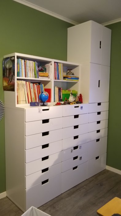 Vit förvaringsmöbel med hyllor och lådor i ett barnrum, med böcker och leksaker.