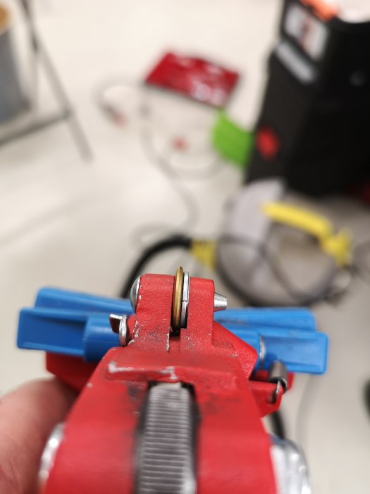 Reparerat handtag på kakelskärare med ny triss och synligt slitage på röd och blå yta.